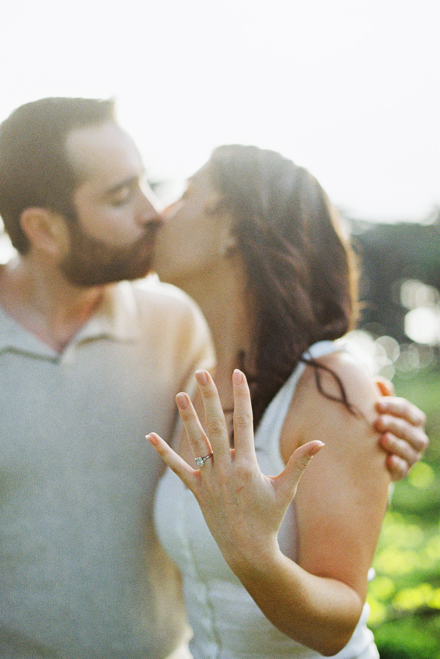Engaged couple sharing a kiss while the woman displays her diamond engagement ring to the camera.