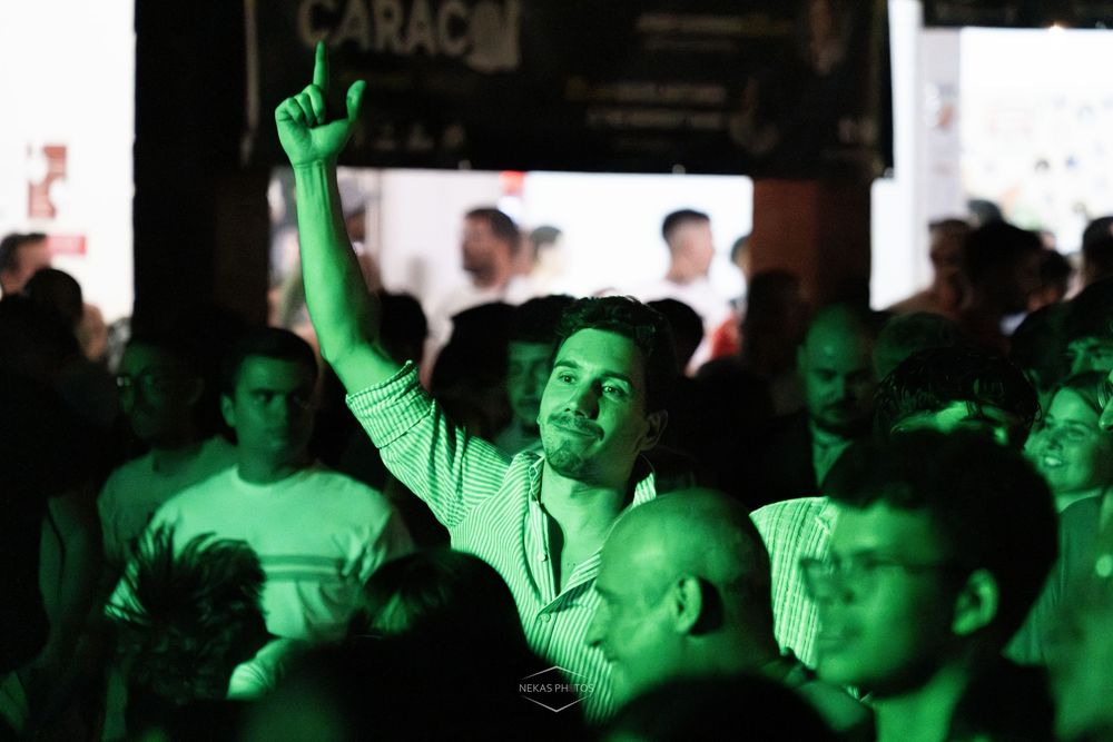 Man raising finger in crowded nightclub bathed in green light.