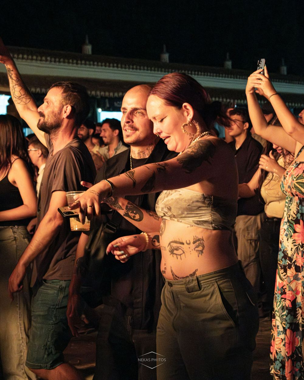 Crowd of people dancing at an outdoor concert, woman with belly tattoos in foreground.