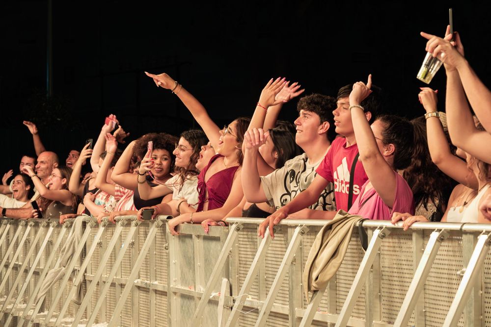 Excited concert crowd cheering with raised arms at an outdoor music festival at night.