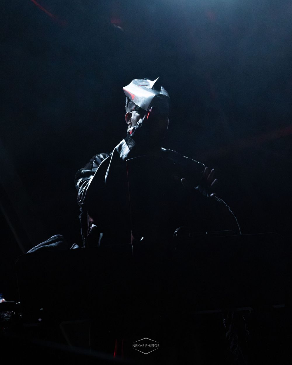 Dark silhouette of a Batman cosplay costume dramatically lit against a black background.