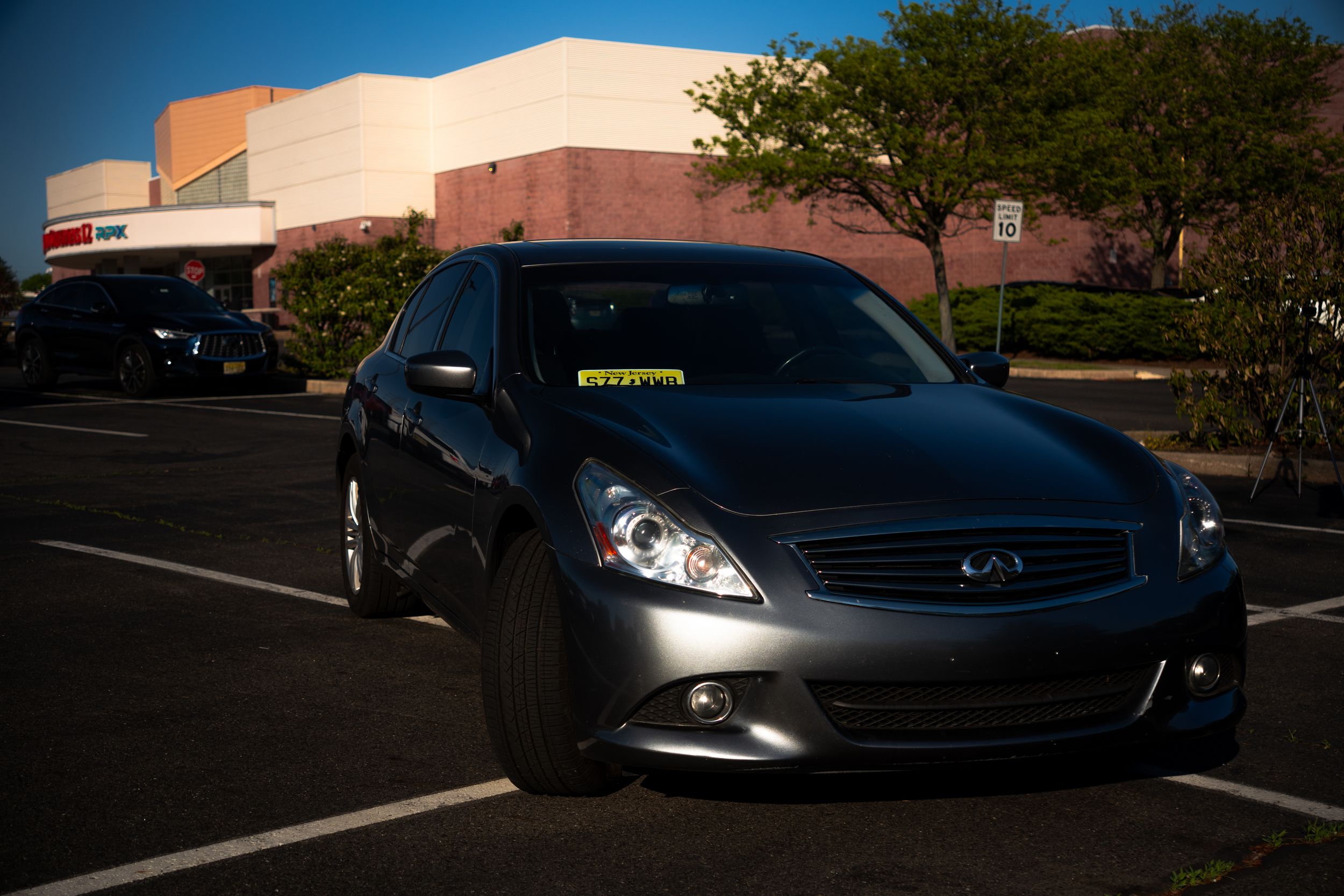 Gray Infiniti G37 sedan parked in sunny commercial parking lot near retail building.