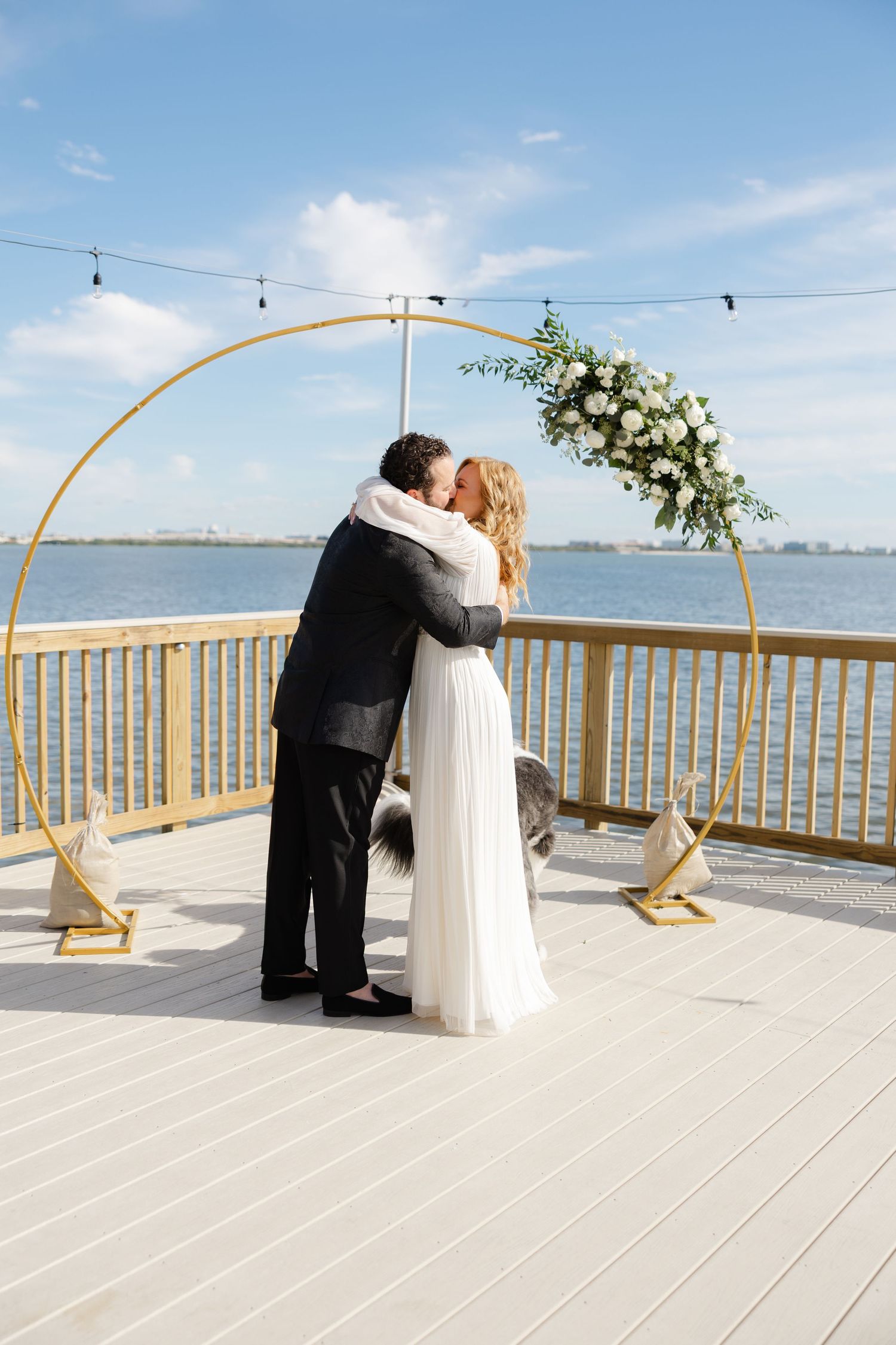 Bride and groom hugging beneath a ceremony arch during a waterfront wedding.