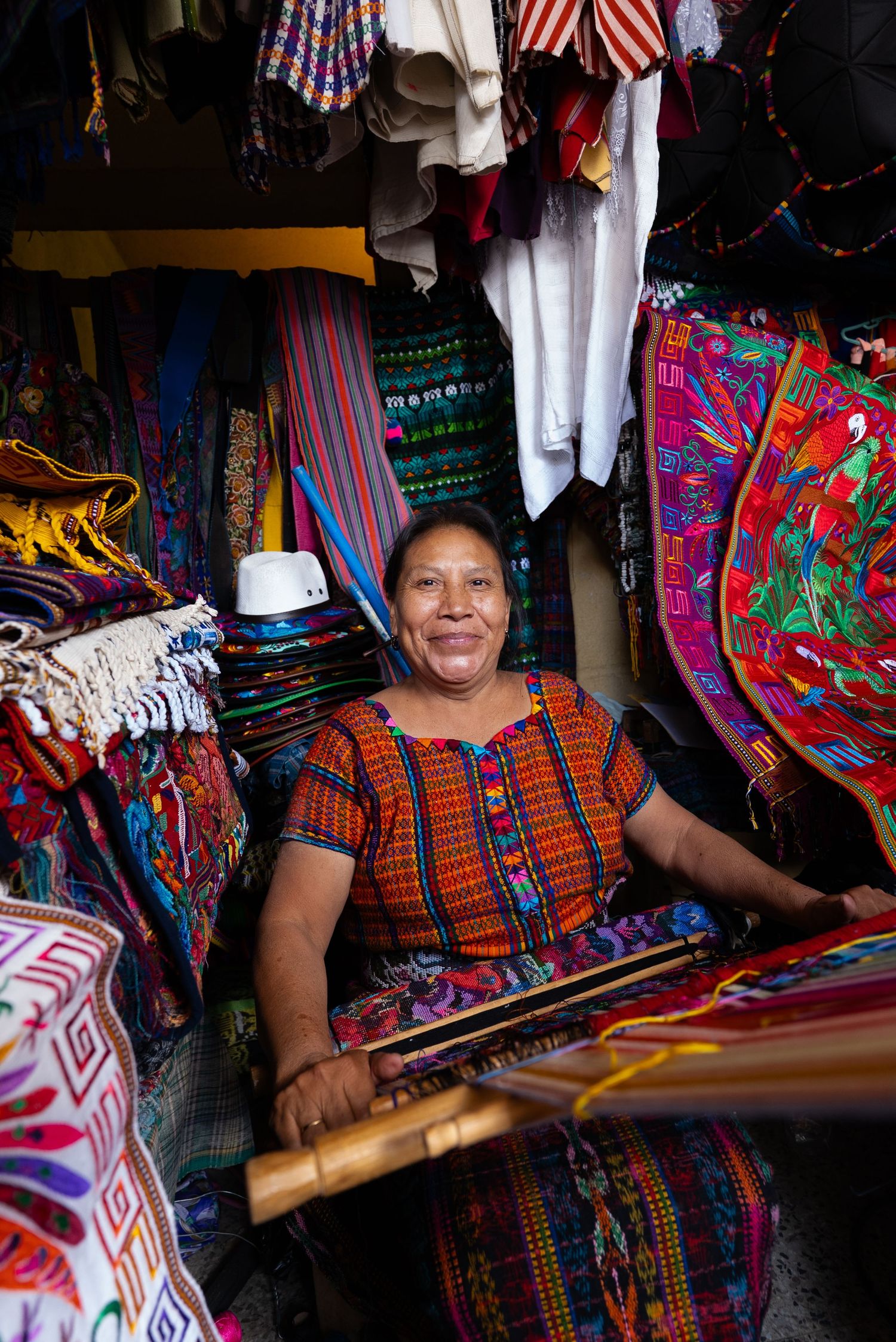 Artisan weaving colorful traditional textiles at a market stall with vibrant fabrics and American flags on display.