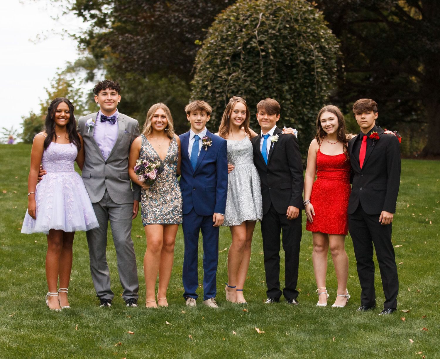 Group of young people dressed formally standing together on grass for a special occasion photo.