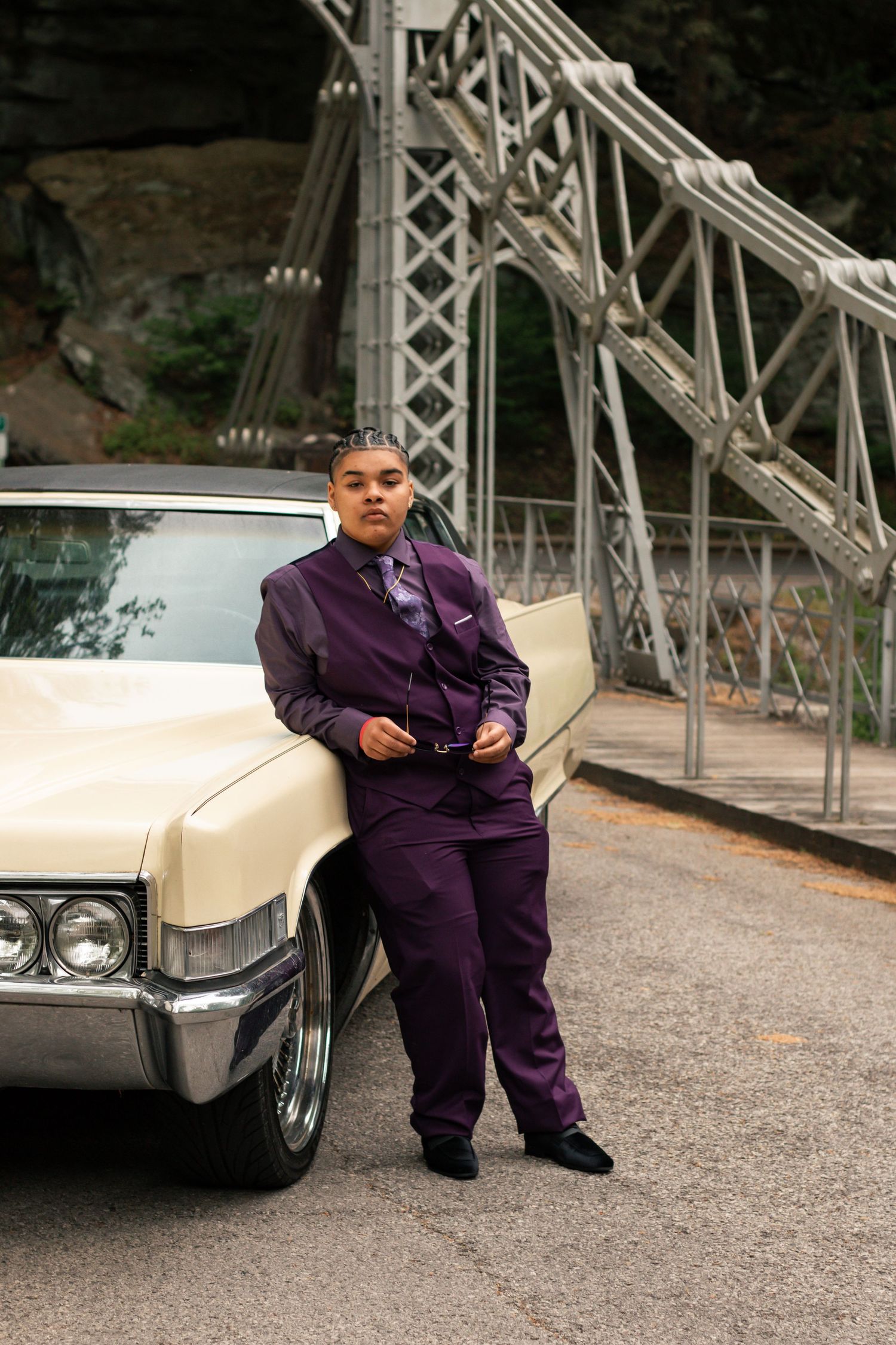 Figure in purple outfit lounges casually beside a classic white car on a paved road. Summer photo sessions Ohio, fall photos in Youngstown,