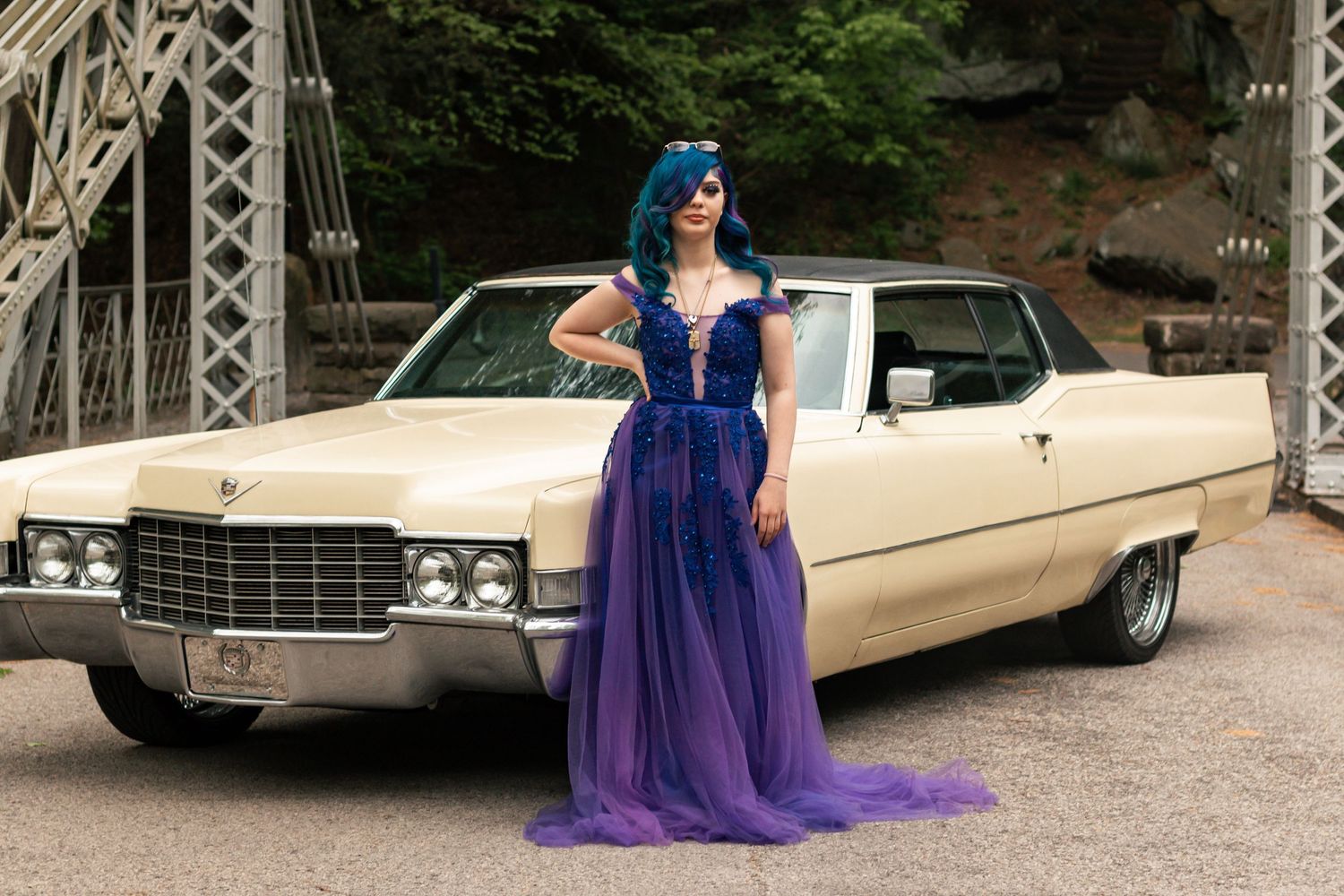 A classic cream-colored Cadillac parked on a bridge with someone wearing a dramatic purple tulle gown standing beside it.Summer photo sessio