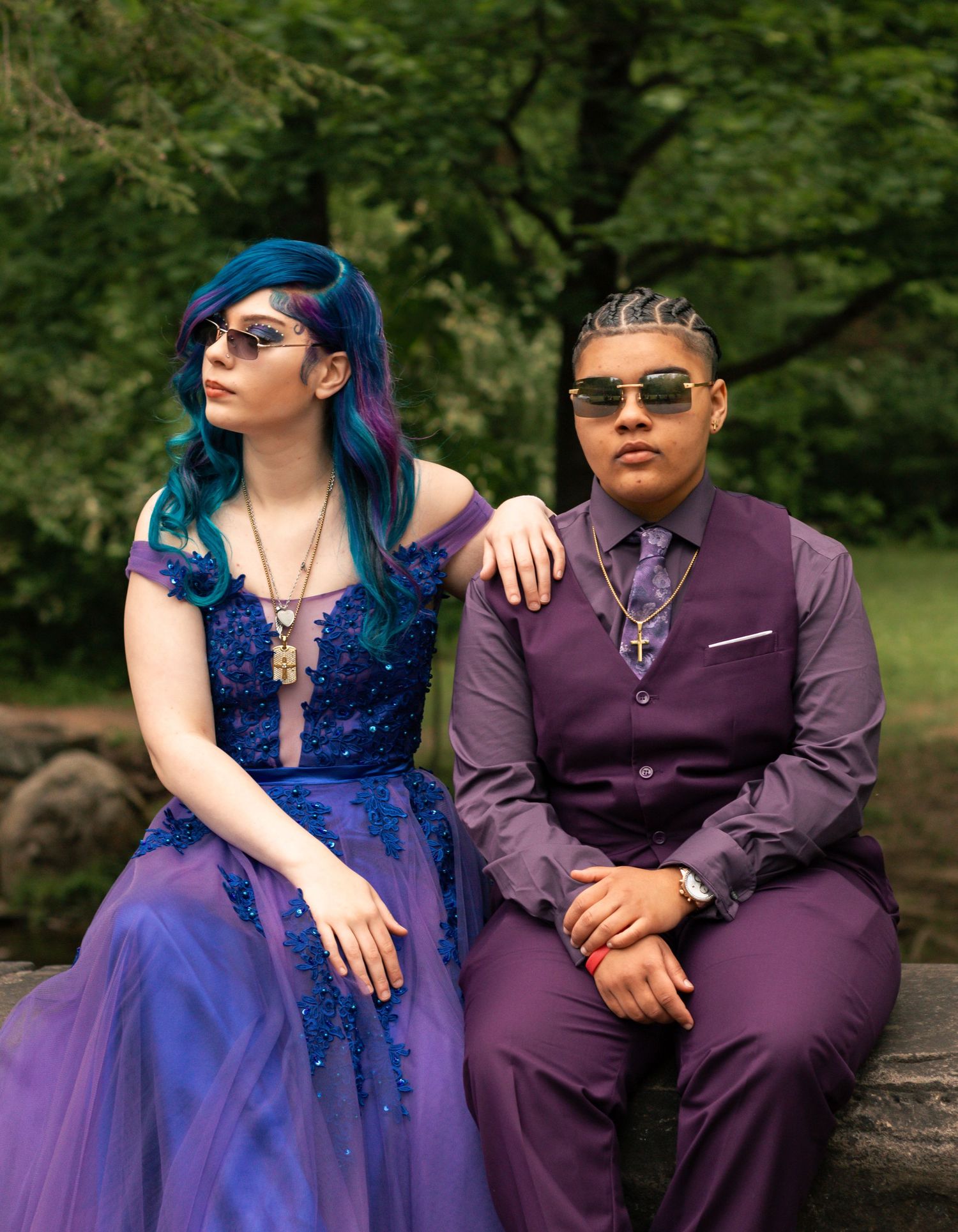 A couple in matching purple and blue formal attire sit together on a stone wall in a garden setting.Summer photo sessions Ohio, fall photos