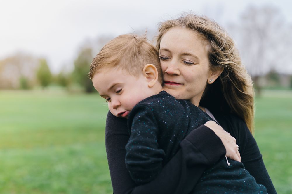 Mother and child sharing a tender embrace outdoors in a green field on a peaceful spring afternoon at Barlow Road Farm Park in Hudson, Ohio.