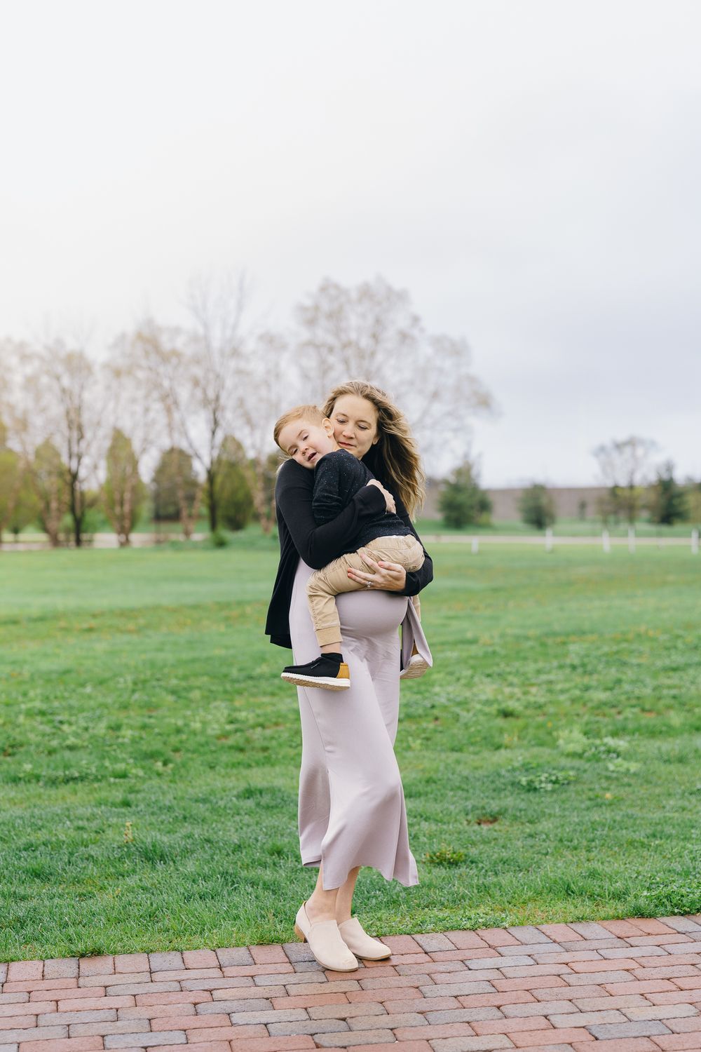 Woman in a pink skirt and black sweater holding a small child on a brick pathway surrounded by green grass at Barlow Road Farm Park in Ohio