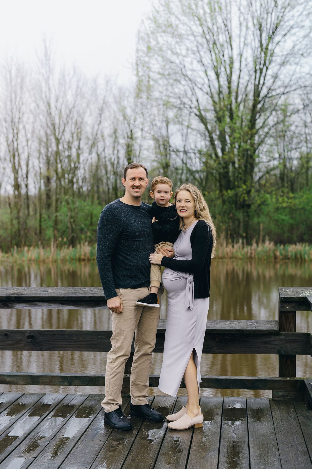 Family poses together on a wooden dock overlooking a serene lake during a spring outdoor photo session at Wood Hollow Metro Park in Hudson.
