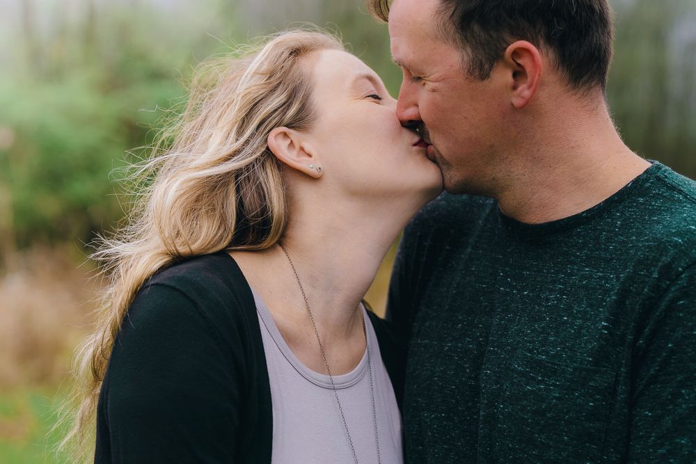 Intimate moment between couple sharing a kiss outdoors in natural setting during maternity session at Wood Hollow Metro Park, Hudson, OH