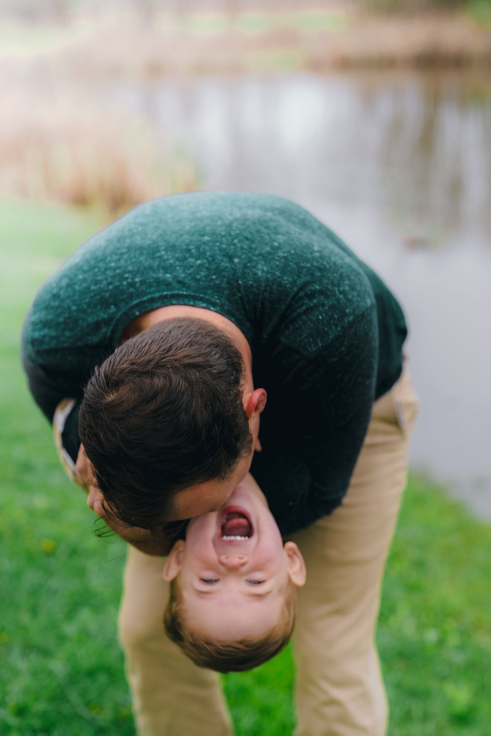 Playful moment captured as parent holds child upside down on grassy area near water at Wood Hollow Metro Park in Hudson Ohio Maternity photo