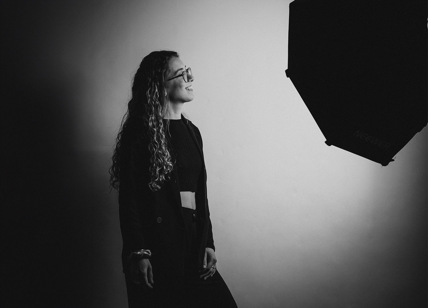 Stylish black and white studio portrait with figure in blazer looking toward an octagonal light modifier.