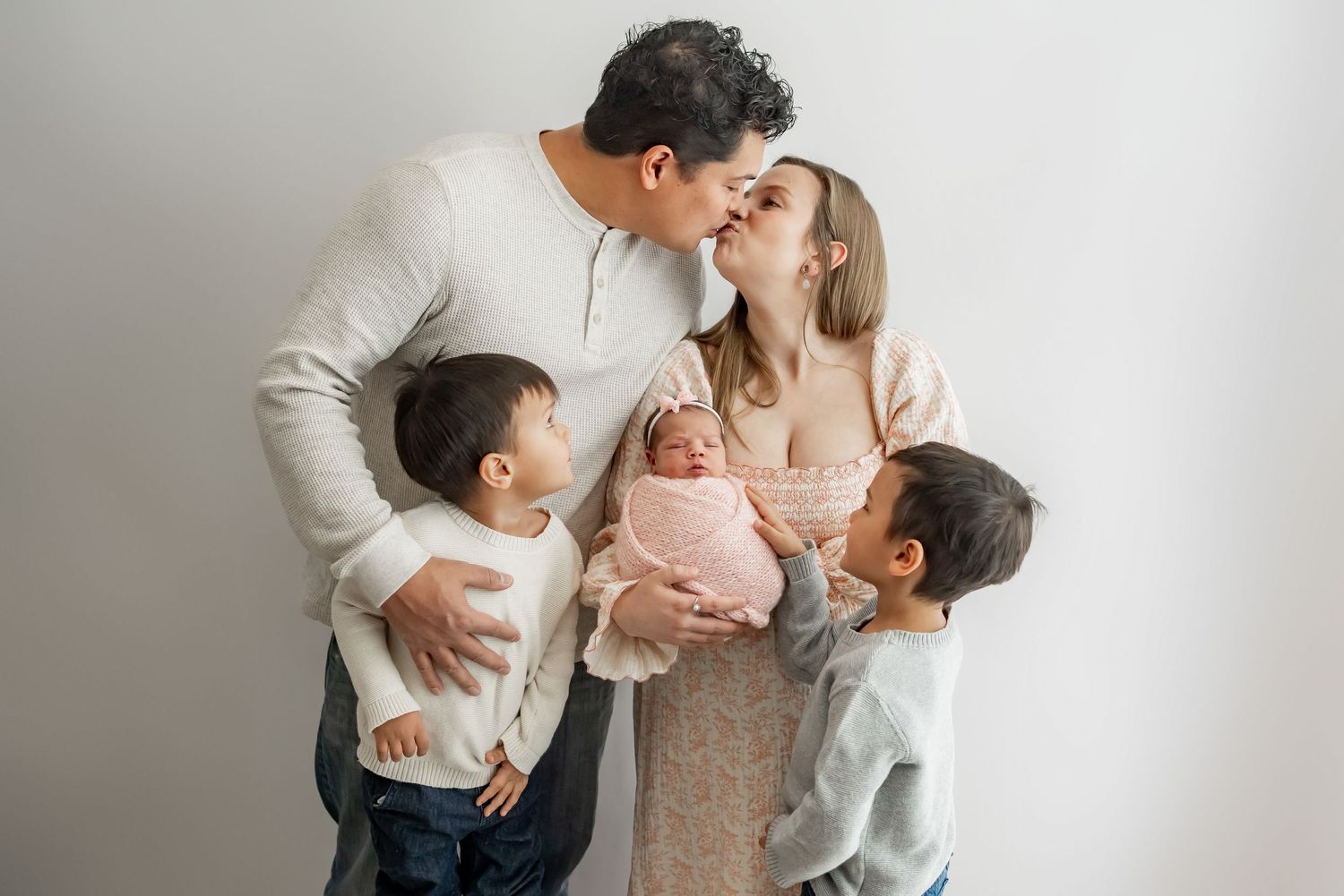 A tender family moment is captured in soft muted tones as they share affectionate embraces together in studio portraits.