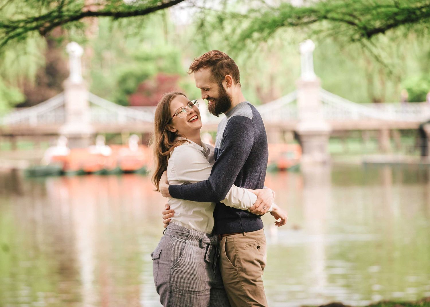 Joyful embrace of couple with Boston Public Garden Foot Bridge and lagoon as romantic backdrop during engagement session