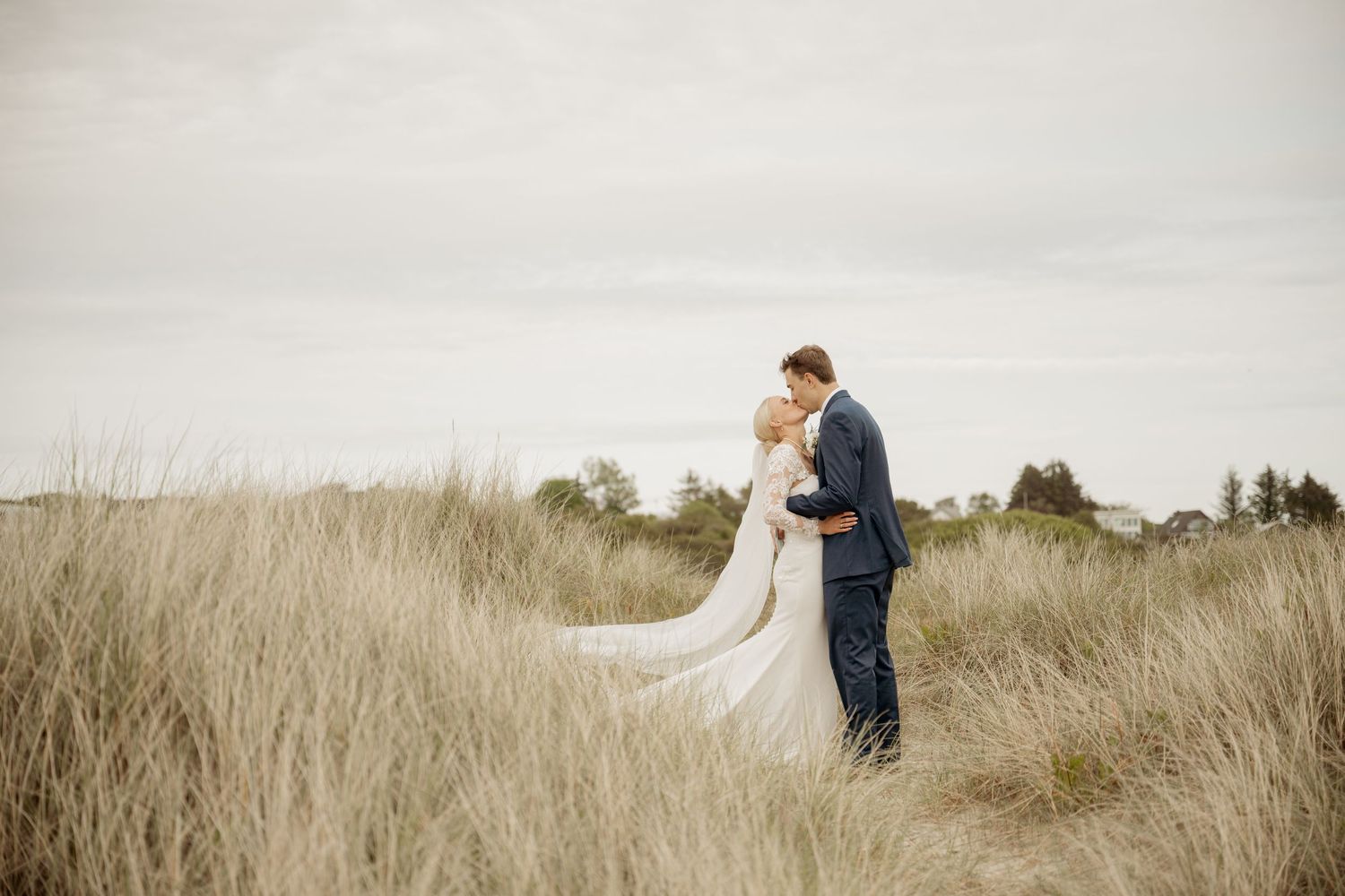 A couple holds hands while spinning together in a snowy field surrounded by winter brush.