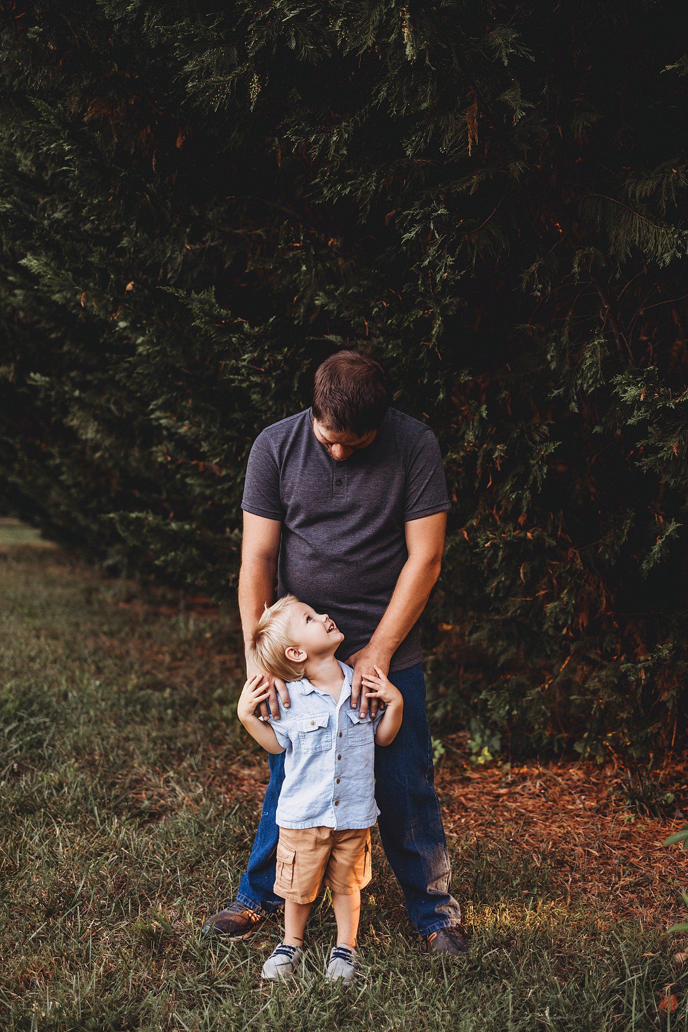 A parent and young child share an intimate moment outdoors surrounded by lush greenery in a candid pose.