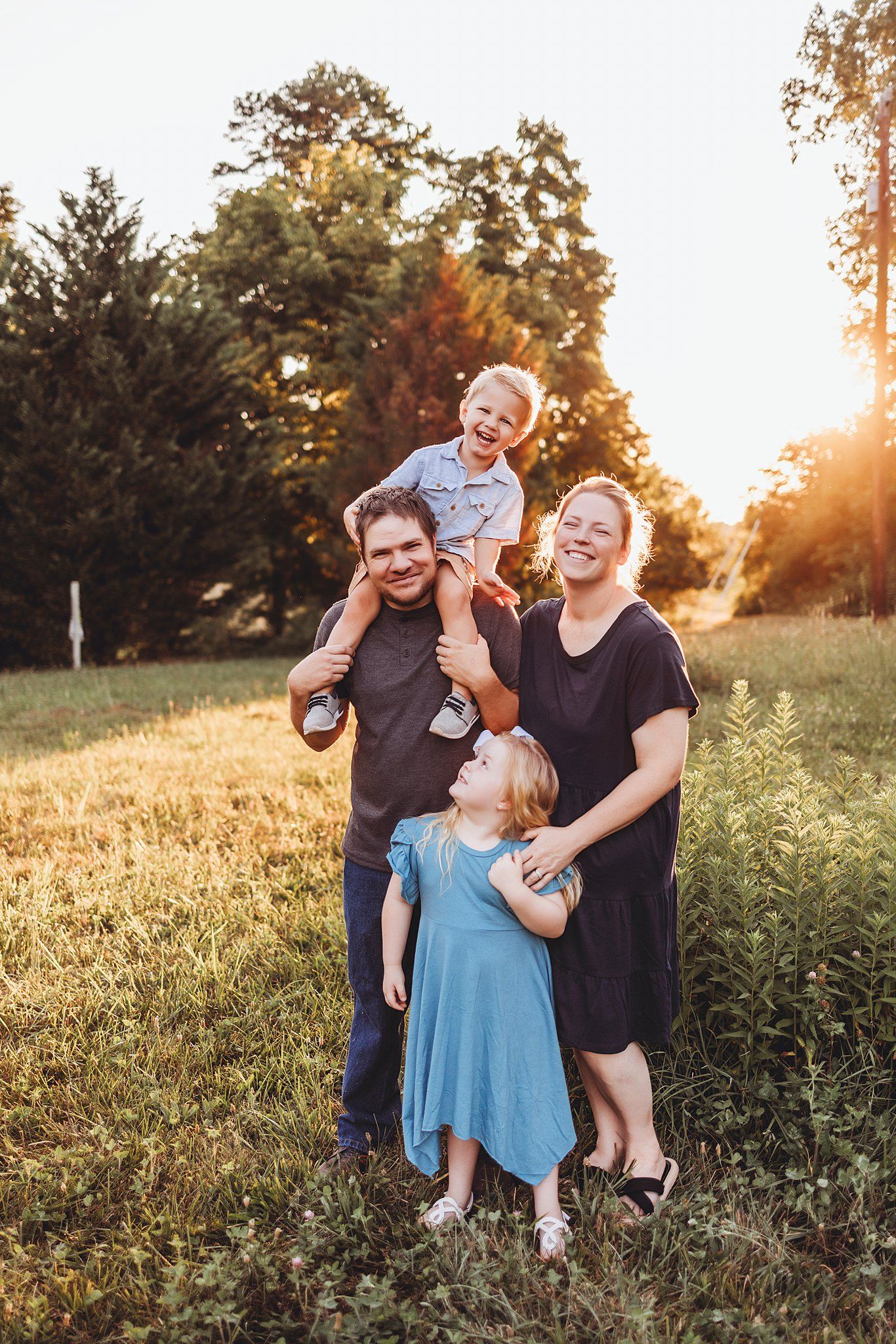 Candid family portrait in golden sunlit field during sunset with children and parents enjoying outdoor moment together.