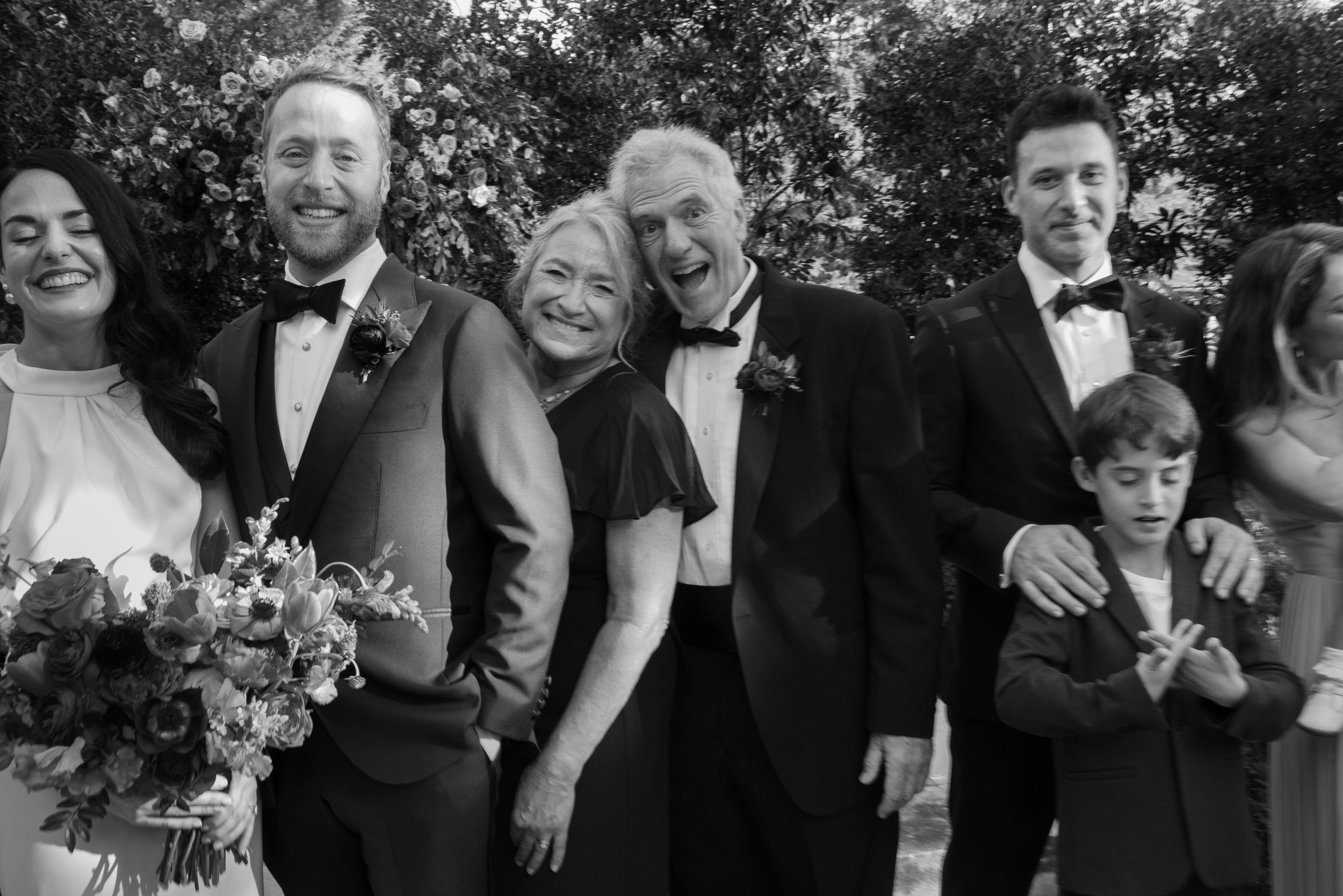 A joyful family poses together outdoors in black and white formal attire with a bouquet of flowers at Belle Meade Historic Site & Winery