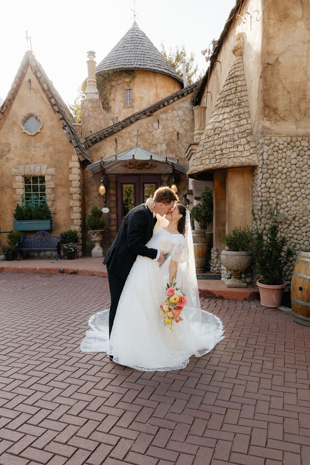 Bride and groom sharing a romantic kiss outside a rustic stone castle wedding venue on a brick courtyard.