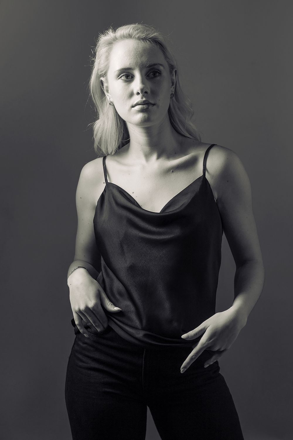 Black and white portrait of a person in dark clothing with light hair against a dark background.
