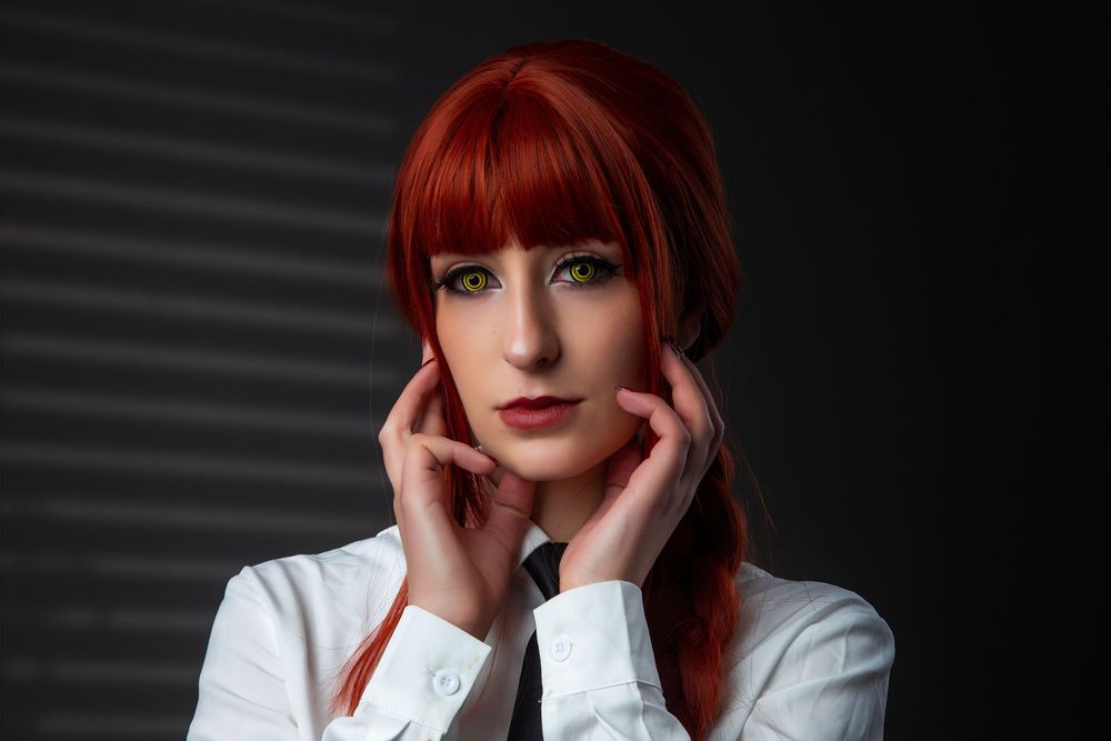 A dramatic portrait of a woman with bright red hair and a white shirt against a dark background.