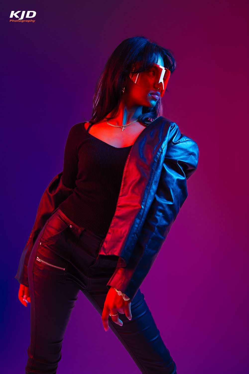 Woman in leather jacket and futuristic glasses poses under dramatic red and blue neon lights.