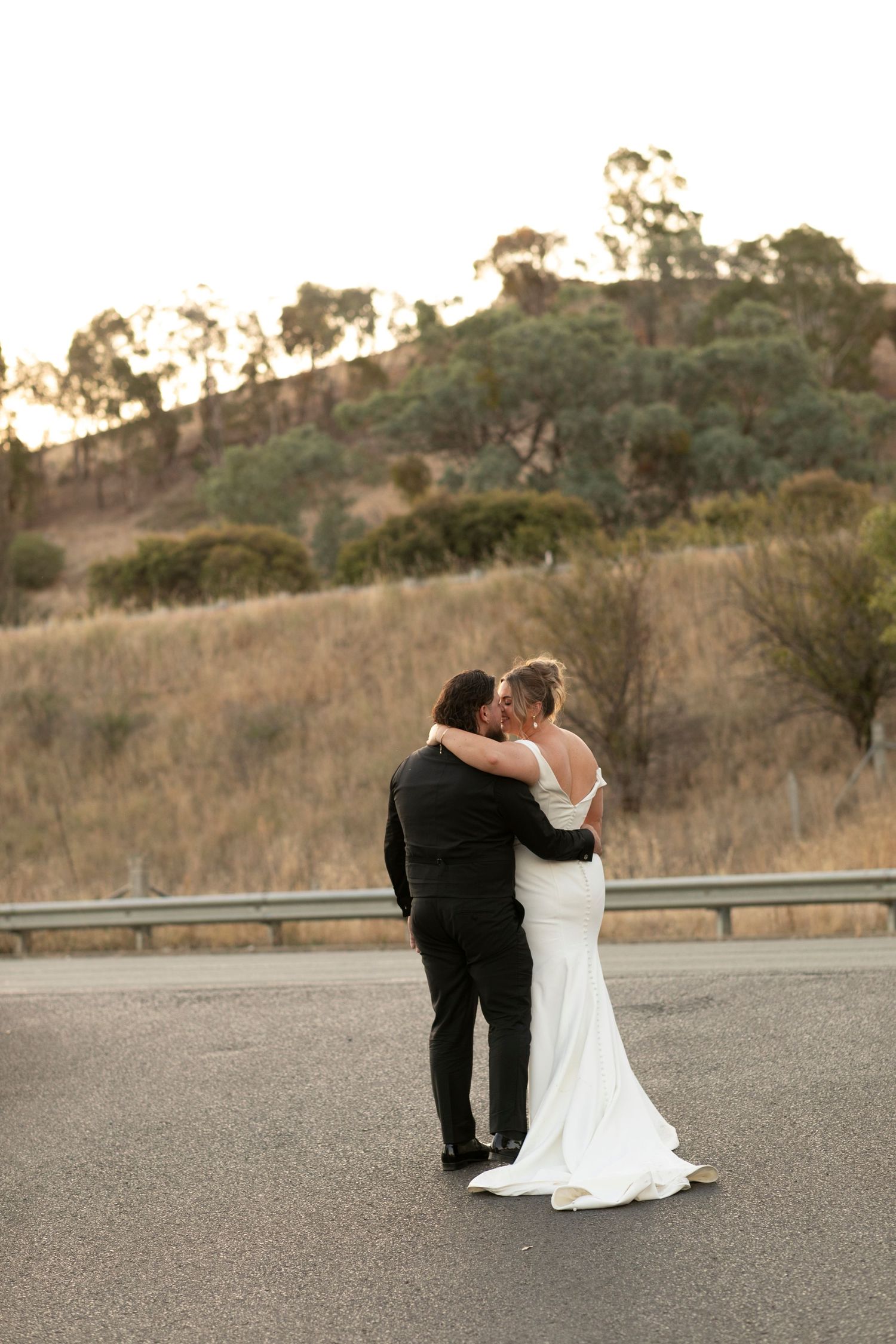 A romantic moment between a couple sitting together on an empty road with hills in the background at sunset.