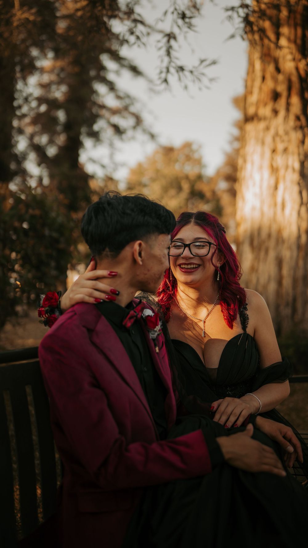 A romantic couple shares an intimate moment on a bench in a sunlit forest setting during golden hour.