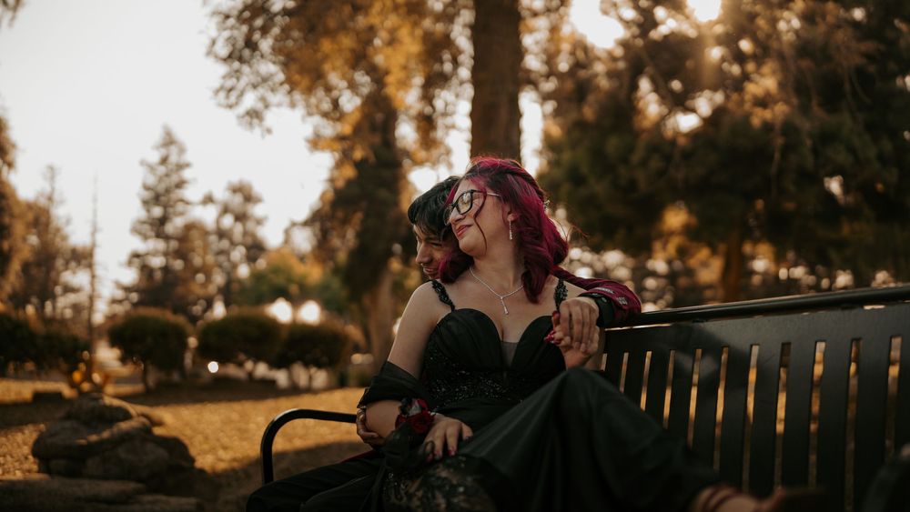 A person in a black dress sits on a park bench at sunset with autumn trees glowing in the golden light.