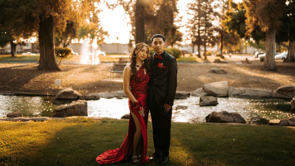 A couple poses together at sunset in a picturesque park with a red dress and formal attire beside a pond.