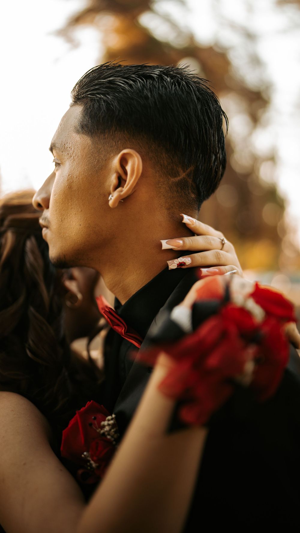 Close-up side profile shot of a couple embracing at golden hour, with red floral details visible.