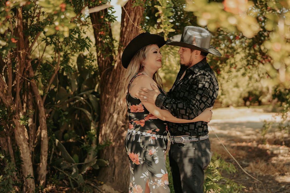 A romantic western-style couple embraces under dappled sunlight in a wooded setting.