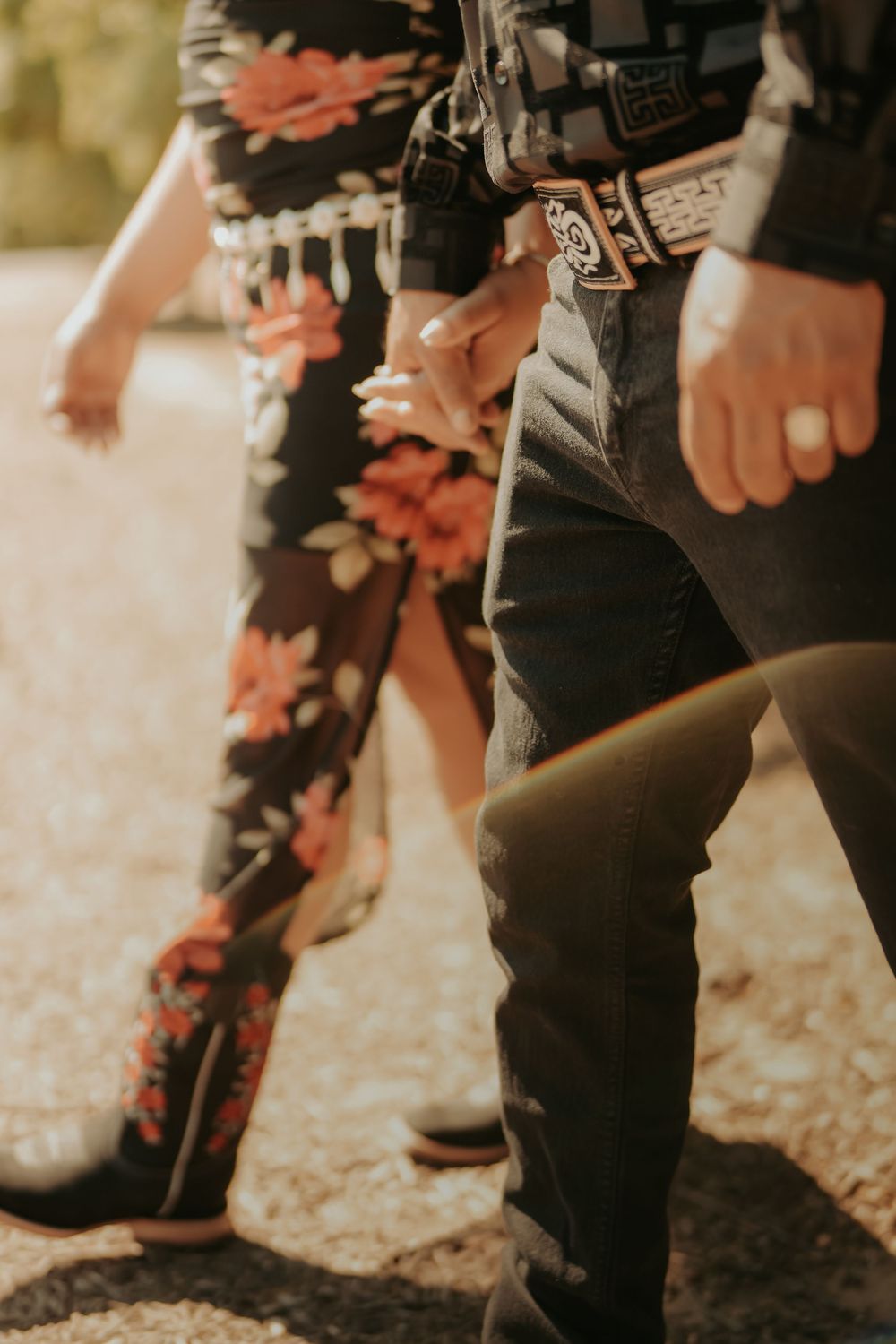 Close-up view of floral patterned pants and dark leather boots on a sunlit ground with autumn leaves.