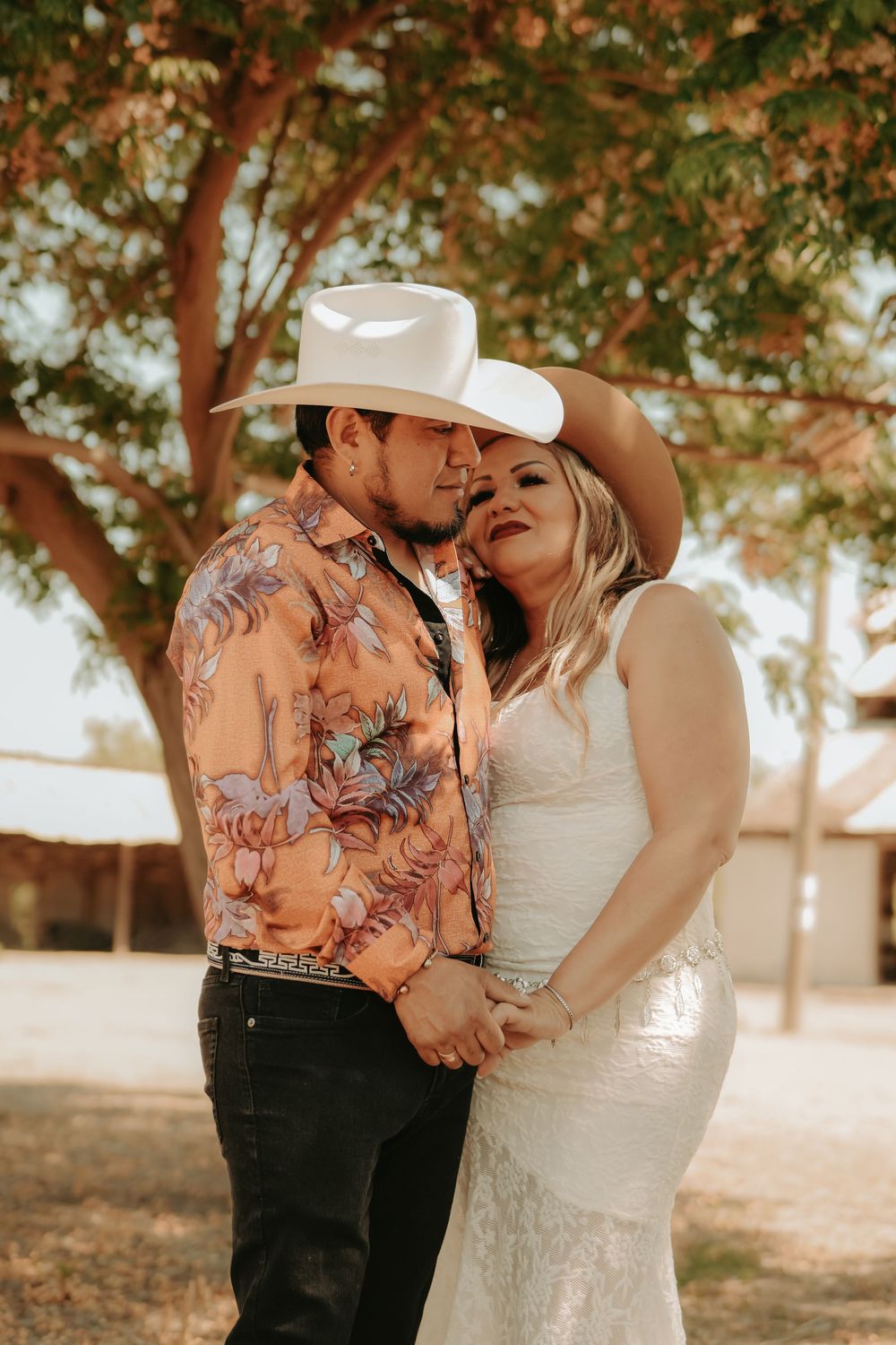 A romantic rustic outdoor wedding photo series featuring a couple in western attire embracing under trees.