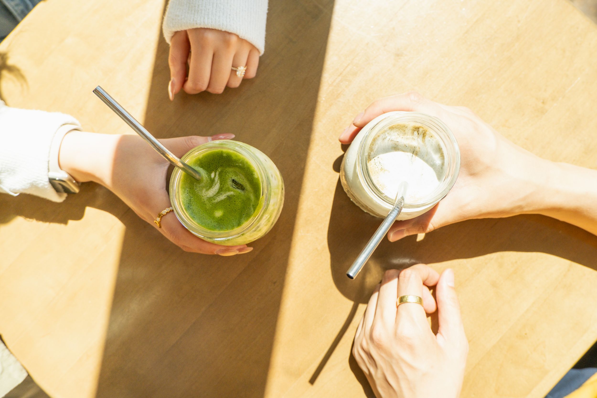 Hands preparing beverages on a wooden surface in warm sunlight.