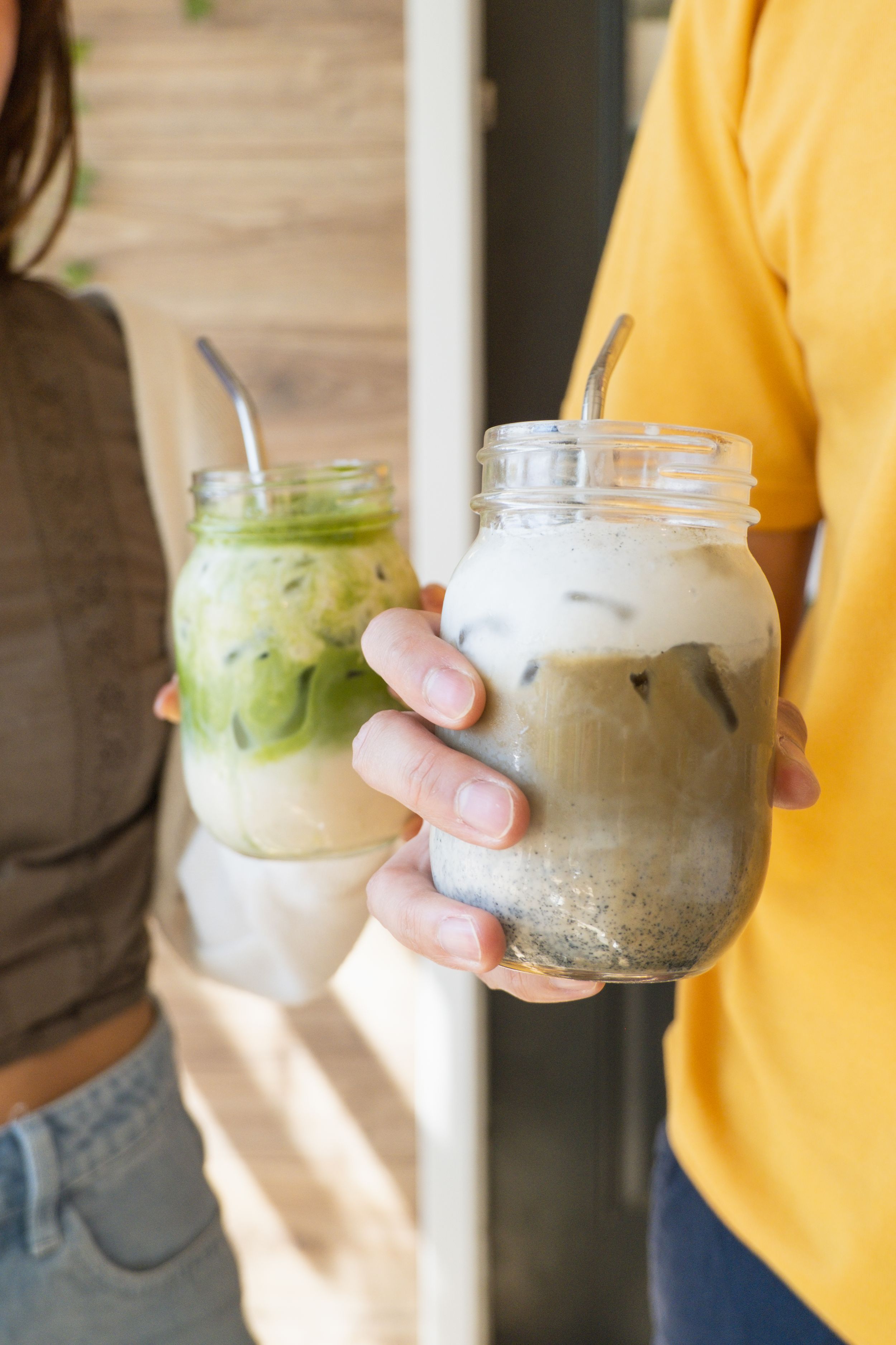 Person in yellow holding various iced drinks in glass jars.