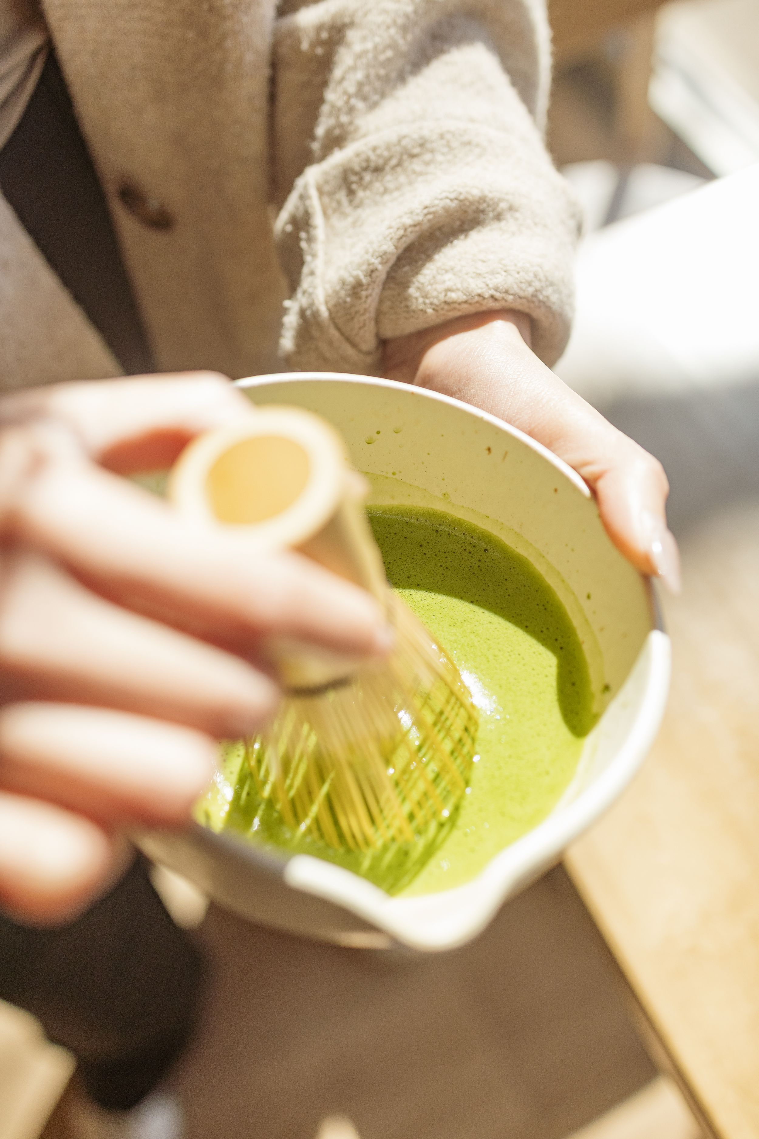 A close-up sequence showing green matcha tea powder being whisked in a traditional ceramic bowl.