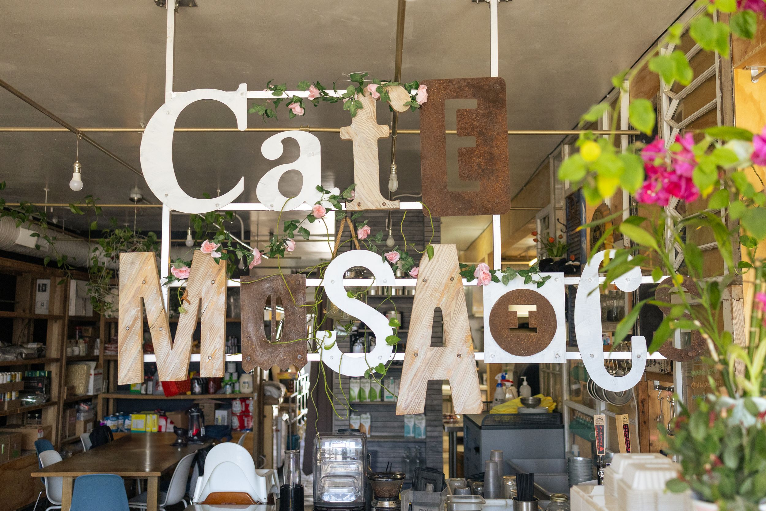 A collection of decorative letters and signs mounted on a wall with greenery and rustic decor in a retail setting.