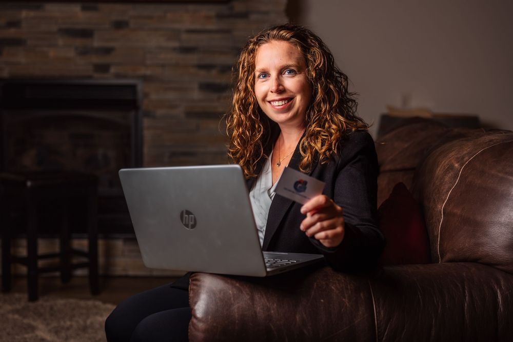 Woman smiling while working on laptop from comfortable leather couch.