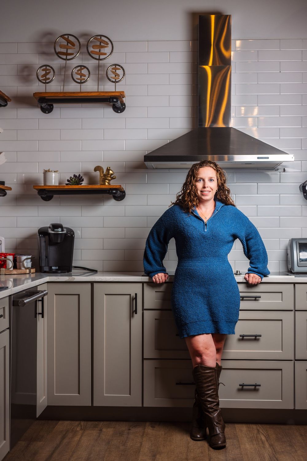 Woman in blue dress posing in modern kitchen with industrial design elements.