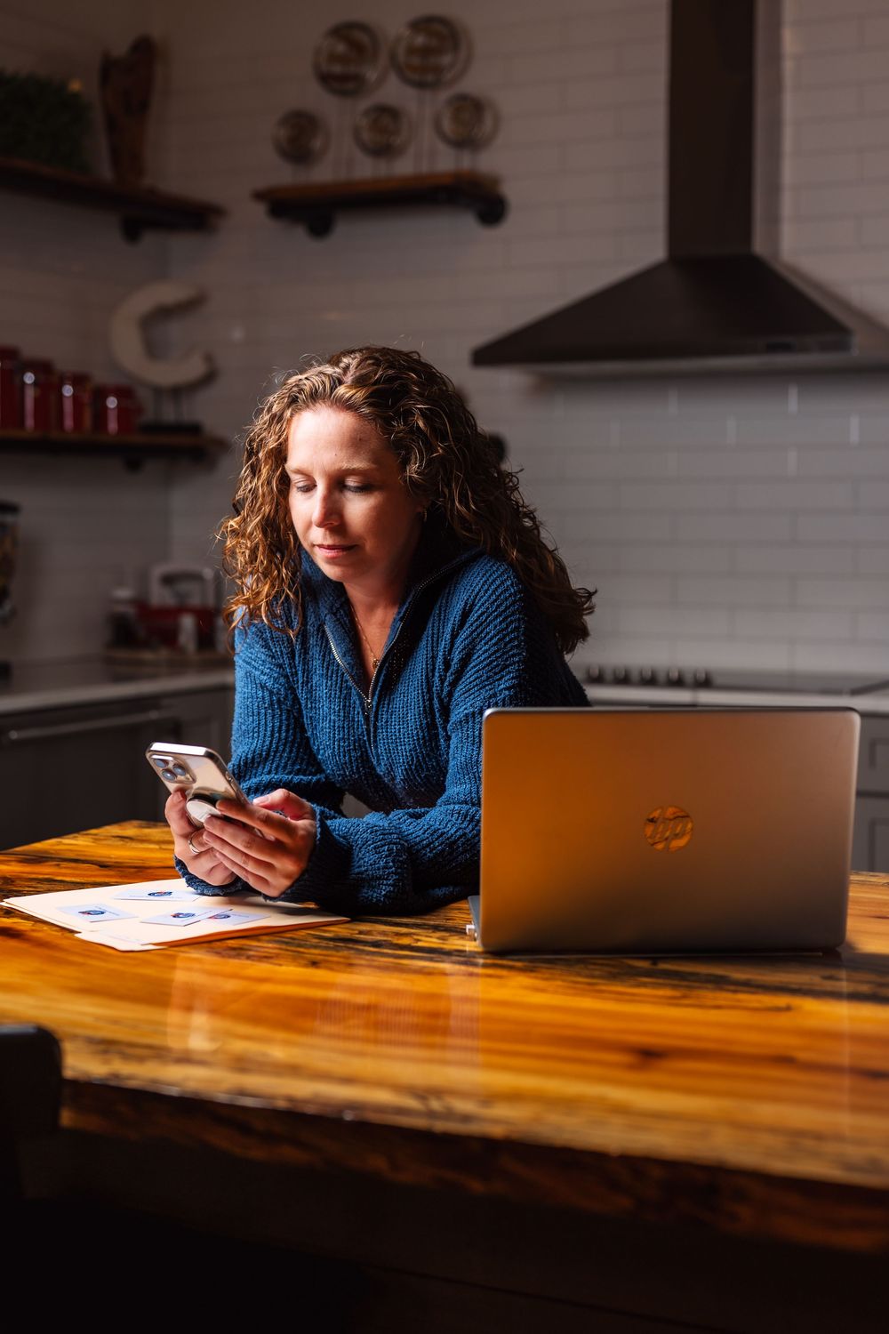 Person in blue sweater sitting at live edge wooden table while checking phone.