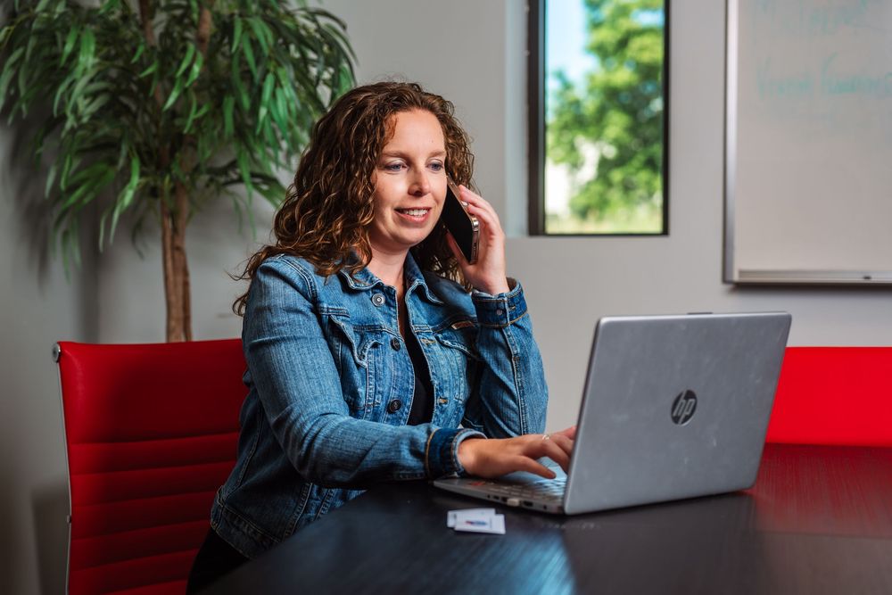 Person in denim jacket working on laptop in bright office space with plants.