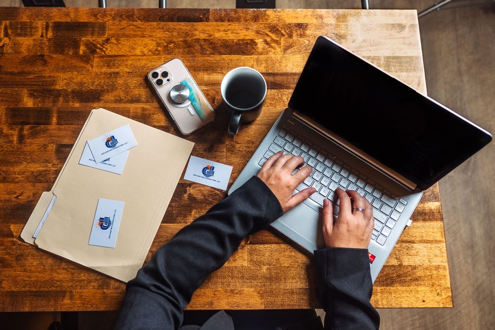 Overhead view of hands typing on laptop keyboard on wooden surface with papers nearby.