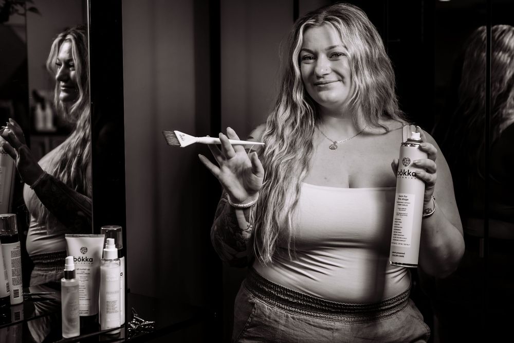 Monochrome portrait showing person demonstrating hair care products in professional setting.