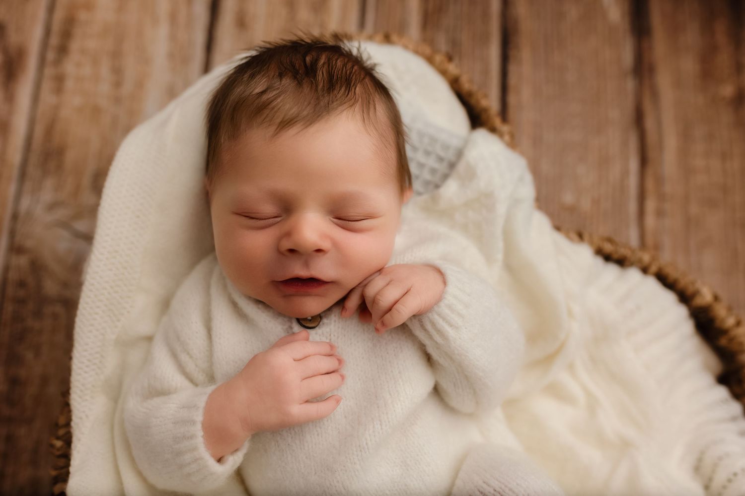 Charlottesville newborn photographer captures a baby boy gently smiling as he sleeps cozily in a heart basket with knits in the studio.
