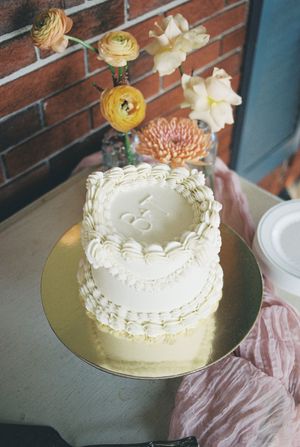 White wedding cake with buttercream details and yellow ranunculus flowers displayed on a gold board.