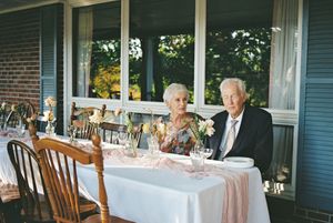 Elderly couple dining together at a formal table setting on an outdoor porch.