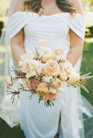 Bridal bouquet with peach roses and delicate florals against white wedding dress.